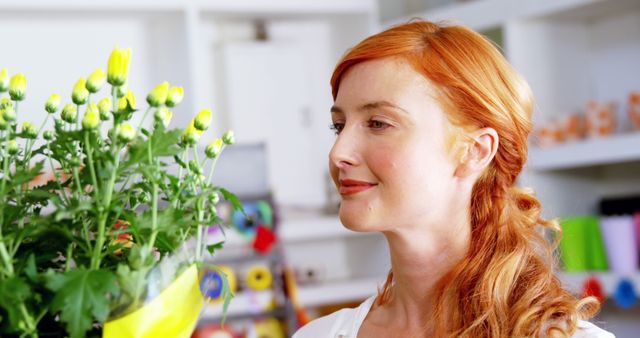 Woman with red hair smiling while enjoying a floral bouquet with yellow flowers. Ideal image for websites and articles focused on floristry, happiness, fragrance, home decoration, or gift-giving.