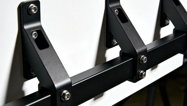 Black metal rail mounting with angled brackets bolting to white panel using hex screws