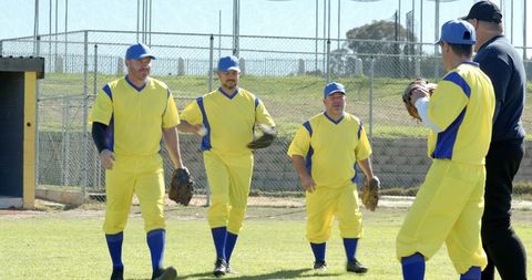 Mature male baseball teammates walking toward camera in bright yellow jerseys on field