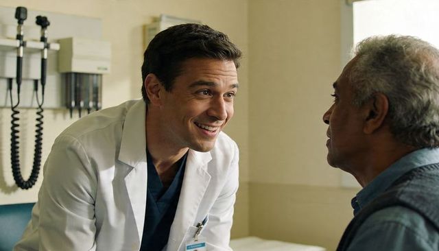 Smiling doctor leaning and speaking with senior patient during clinic consultation and exam