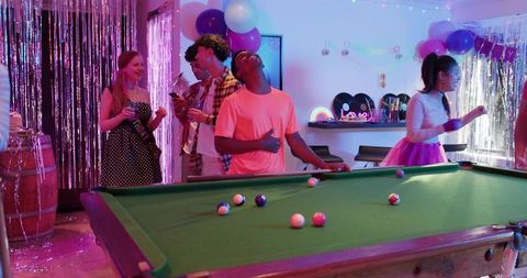 Diverse friends celebrating neon-lit pool table party with retro vinyl decor and tutu
