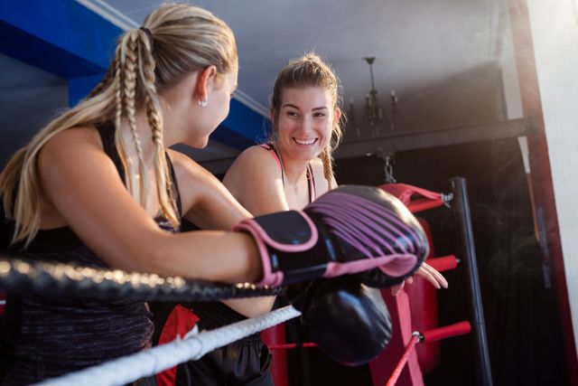 Two women sharing a moment in a boxing ring, representing teamwork and motivation in sports training. Ideal for fitness blogs, sports articles, and advertising gym memberships or training programs.