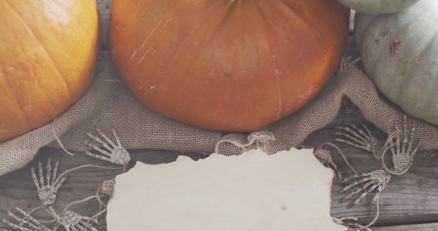 Pumpkin display with skeleton hands and antique paper creates a rustic Halloween setting. Ideal for Halloween cards, party invitations, seasonal decorations, and autumn-themed promotions.