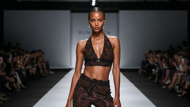 Confident model walking runway in halter crop top and belted patterned trousers