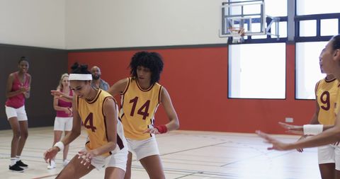 Female basketball team training with coach on indoor court