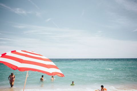 Red white striped umbrella over turquoise ocean with swimmers relaxing on sunny shore