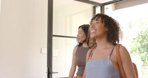 Smiling diverse women entering modern bright foyer through black framed glass door