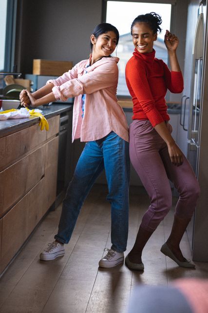Full length of cheerful biracial mother and daughter dancing in kitchen, copy space. Unaltered, family, love, together, enjoyment, lifestyle and home concept.