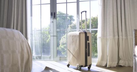 Modern gold suitcase in sunlit room by large glass doors