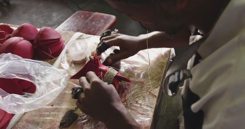 Young African American man focusing on sewing fabric in a workshop suggests detailed craftsmanship and concentration. Suitable for depicting handmade processes, artisanal craft skills, or highlighting small-scale manufacturing artistry.