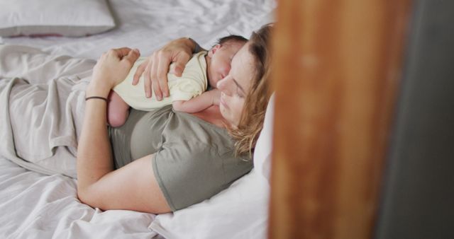Mother is cuddling and holding her newborn baby close while lying in bed. Perfect for themes of maternal love, new babies, parenthood, family bonding, and gentle affection. Ideal for articles, blogs, parenting magazines, and baby product advertisements.