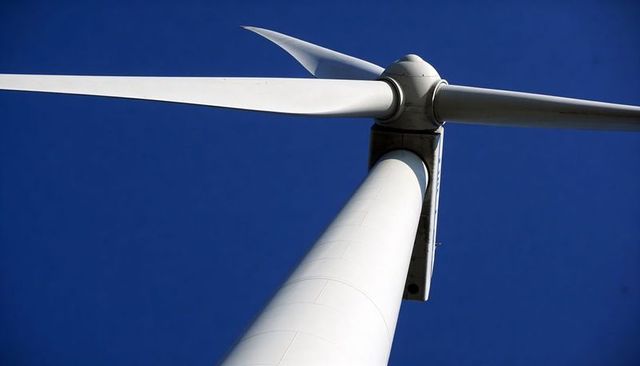 Low-angle wind turbine tower blade against deep blue sky generating clean modern energy