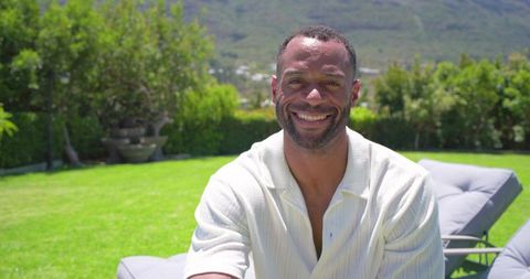 Smiling african american man relaxing on cushioned lounge chair in sunny backyard garden