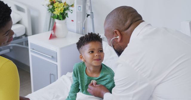 A doctor in white coat examining a joyful young boy while his mother observes lovingly in a hospital room. Bright and cheerful setting with decorative flowers in background. Ideal for health-related websites, patient care brochures, family health services promotion, and pediatric care advertisements.