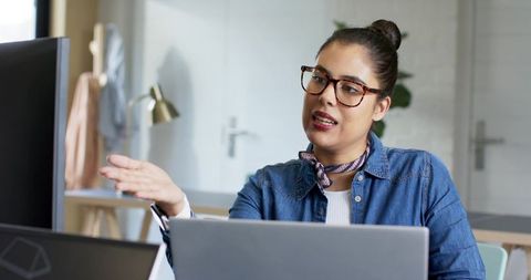 Female professional gesturing while discussing project at modern coworking desk with laptop