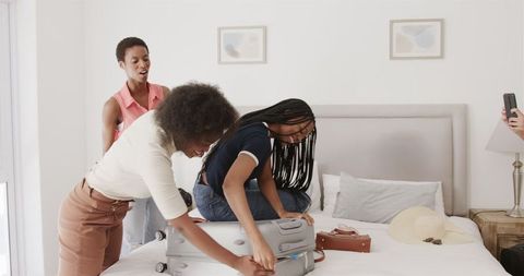 Joyful African American Friends Packing for Vacation on Bed