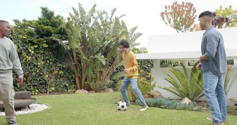 Friends playing backyard soccer on lawn with tropical garden and modern fire pit