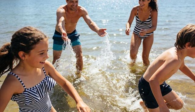 Family splashing in shallow beach water on sunny summer day, kids and parents playing