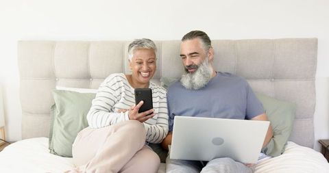 Senior Couple Sharing Smartphone On Bed For Modern Connectivity