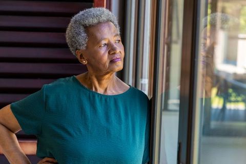 Contemplative african senior woman gazing through sliding glass door showing quiet strength