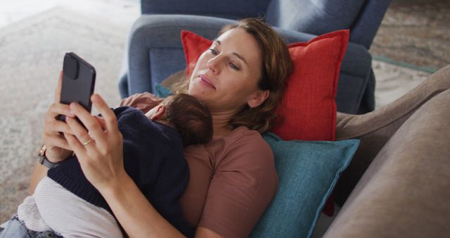 Image of caucasian mother with smartphone lying on sofa with newborn sleeping baby - Download Free Stock Photos Pikwizard.com