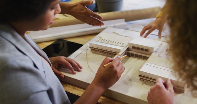 Architects adjusting a scale model of modern building with focused attention, highlighting aspects related to architecture, teamwork, and project development. Useful for articles or promotional content related to architecture firms, engineering schools, construction projects, and design collaboration.