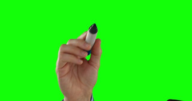A Caucasian hand is holding a marker against a green screen background, with copy space. Ideal for presentations or educational content, the green screen allows for easy background replacement or graphic overlays.