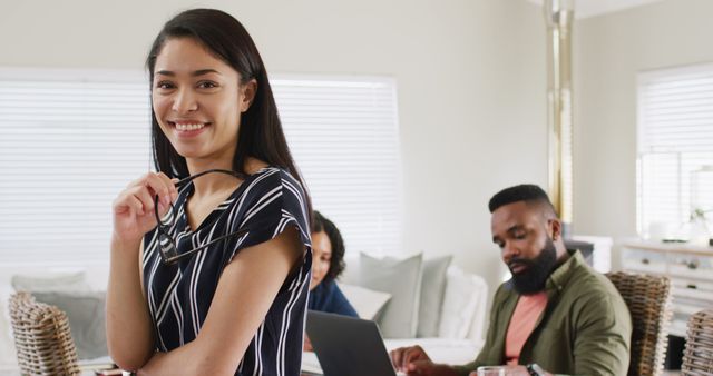 Smiling Woman Holding Glasses with Coworkers Working in Background - Download Free Stock Images Pikwizard.com