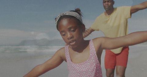Balancing girl on shore with parent mimicking playful movement at sunny beach