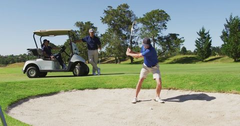 Senior golfer hits ball from sand trap on sunny day