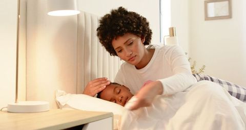 Mother tenderly tucking sleeping child in cozy bedroom