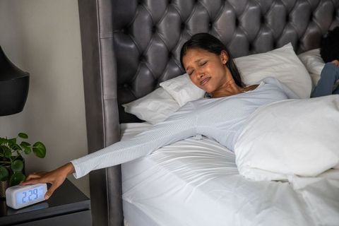 Woman reaching for alarm clock from cozy bed