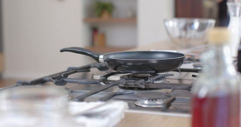 Black nonstick frying pan sitting on modern gas cooktop over wood counter with soft bokeh