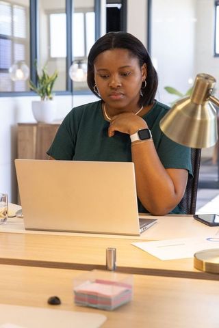 African american woman working on laptop at modern bright office desk, focused