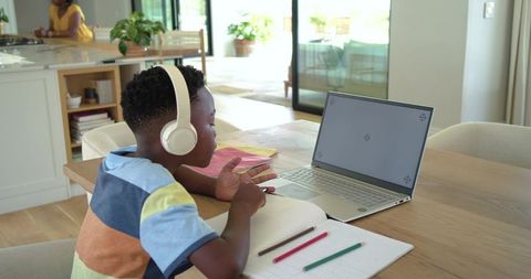 African american boy studying at home on laptop with headphones during remote learning