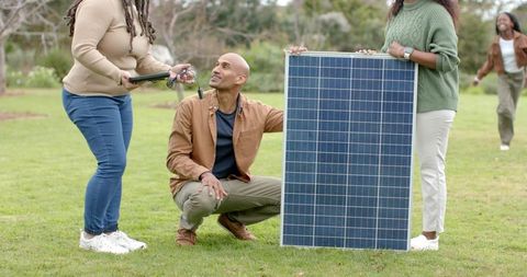 Multigenerational diverse family examining freestanding solar panel on park lawn together