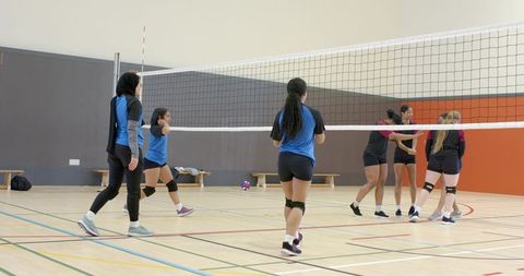 Indoor youth female volleyball teams competing across net with teamwork, diversity, hijab