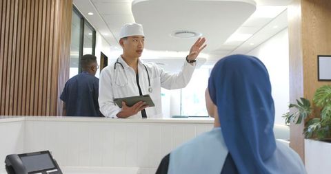 Asian doctor consulting with receptionist at modern clinic reception desk using tablet