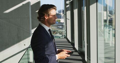 Businessman Using Smartphone in Sunlit Office Corridor