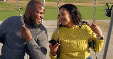 Happy Couple Interacting on Park Swings During Sunny Day - Download Free Stock Images Pikwizard.com