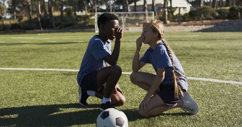 Kneeling teammates whispering strategy on soccer field with ball for youth teamwork