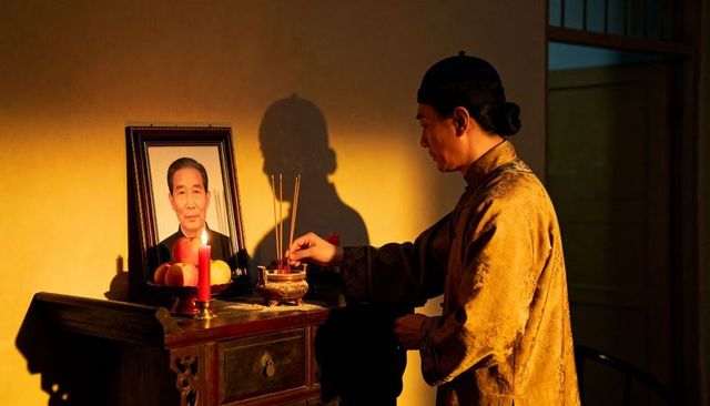 Placing incense at traditional home altar with ancestor portrait and candle offering