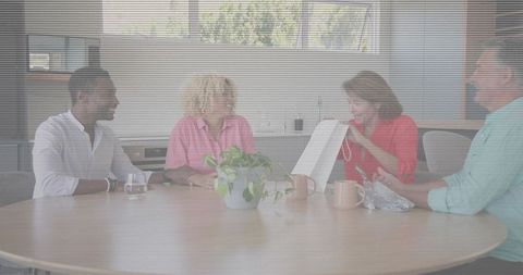 Diverse team sharing gift at roundtable meeting in bright workspace with plant and coffee