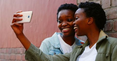 Smiling Twin Sisters Taking Selfie Against Brick Wall