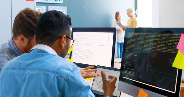 Image of young programmers collaborating on a software development project in a modern office. They are working on code on multiple computer screens and a tablet. Ideal for use in articles or marketing materials about technology, coding, software projects, teamwork, or modern work environments.
