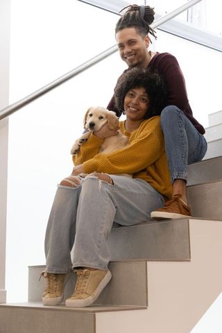 African american couple sitting on stairs cuddling golden retriever puppy in modern home