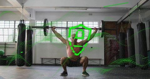 Athlete performing deep overhead squat with barbell in boxing gym with green digital overlay