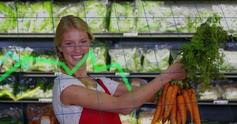 Smiling produce clerk holding fresh carrots in cold aisle with green sales graph overlay
