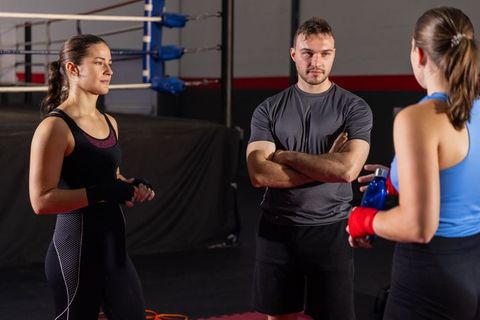 Boxing coach guiding two female boxers during intense training session at gym ring