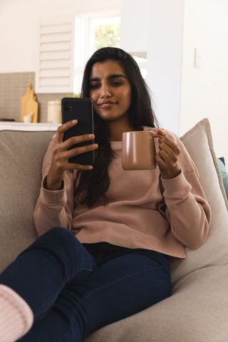 Woman Relaxing at Home with Smartphone and Coffee Mug